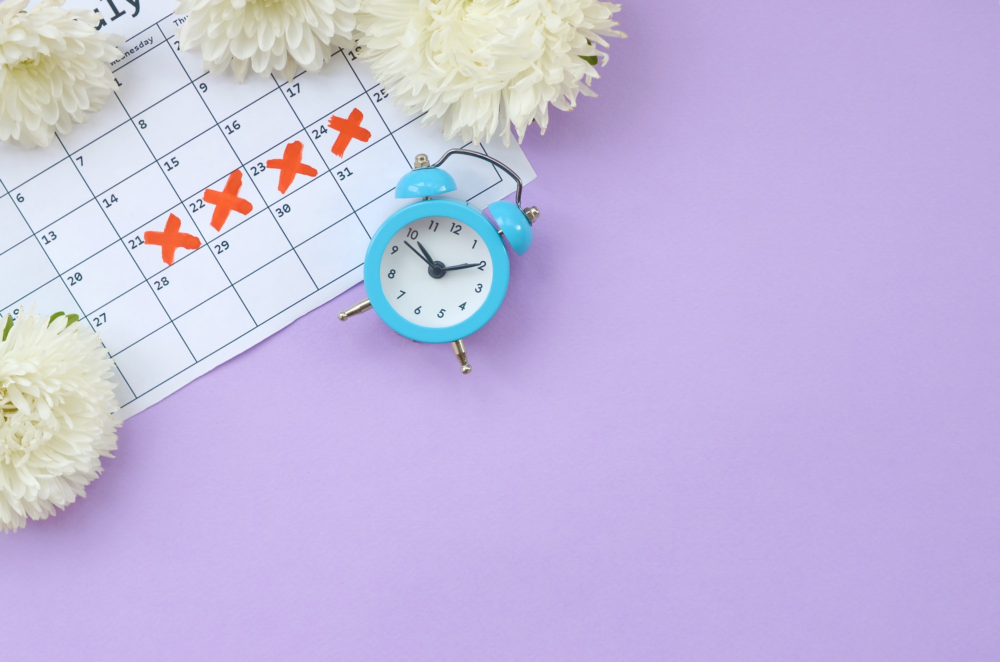 Blue alarm clock and white flowers on menstrual period calendar with red cross marks