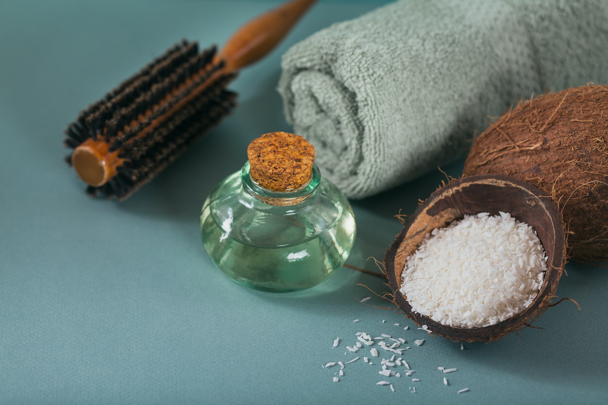 Coconut oil in a bottle with coconuts, towel and hairbrush on light blue background